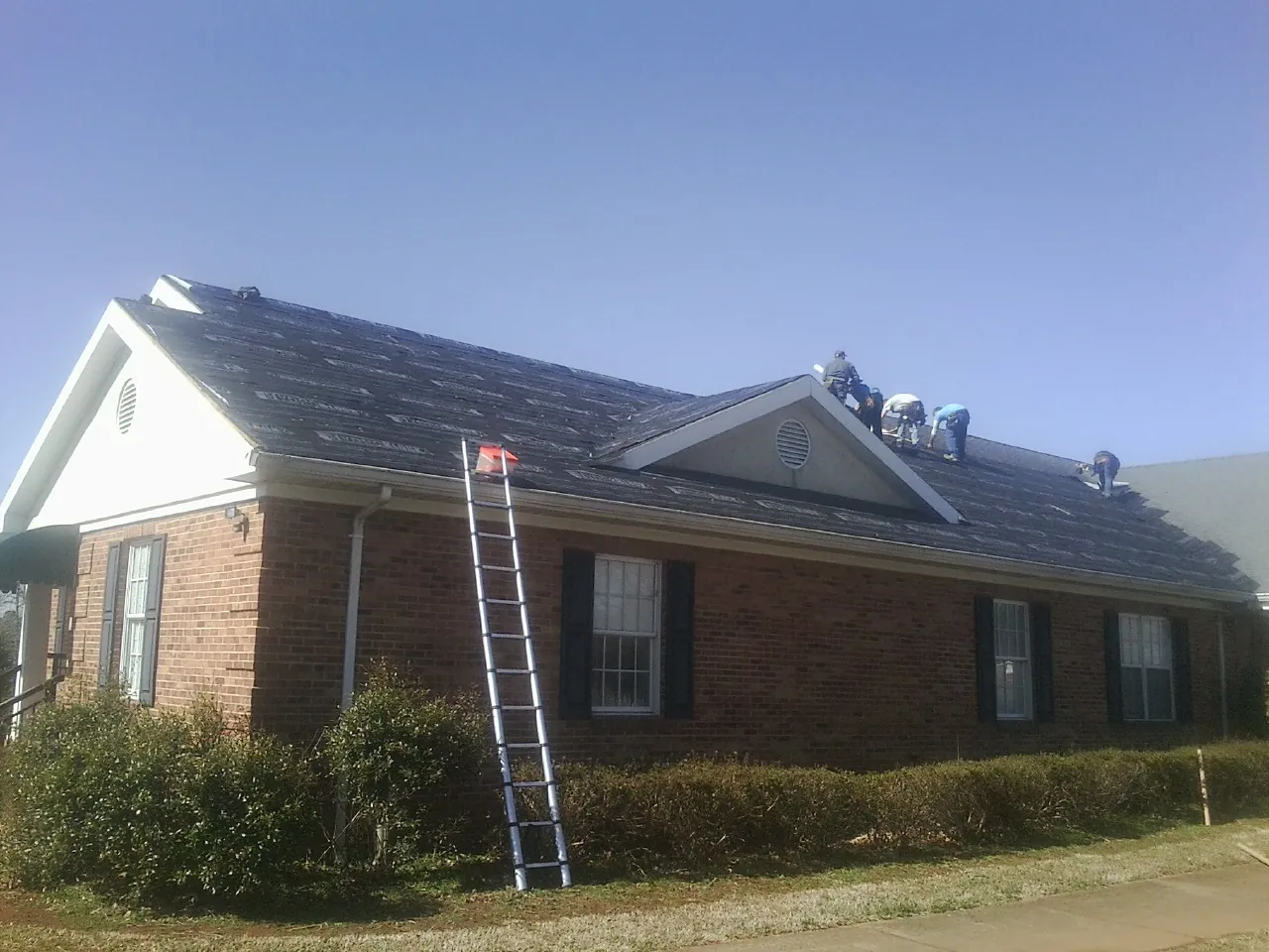 Crew tearing shingles off a brick ranch roof with a ladder set — Emergency Roof Repair work by our crew in Jim Thorpe
