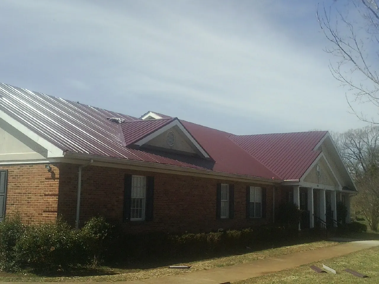 Red metal roof with gabled entries on a long brick building, from a Hail Damage Roof Repair job in Jim Thorpe