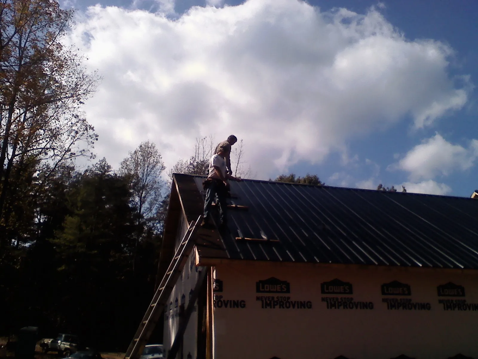 Roofer fastening dark metal panels high against a cloudy sky, from a Roof Inspection job in Jim Thorpe