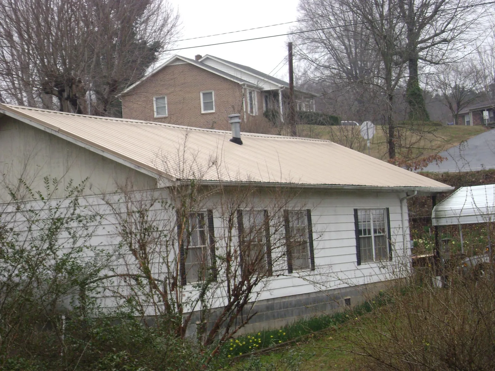 Tan metal roof on a white sided house set into a hillside — Commercial Roofing by Roofing Brothers in Jim Thorpe
